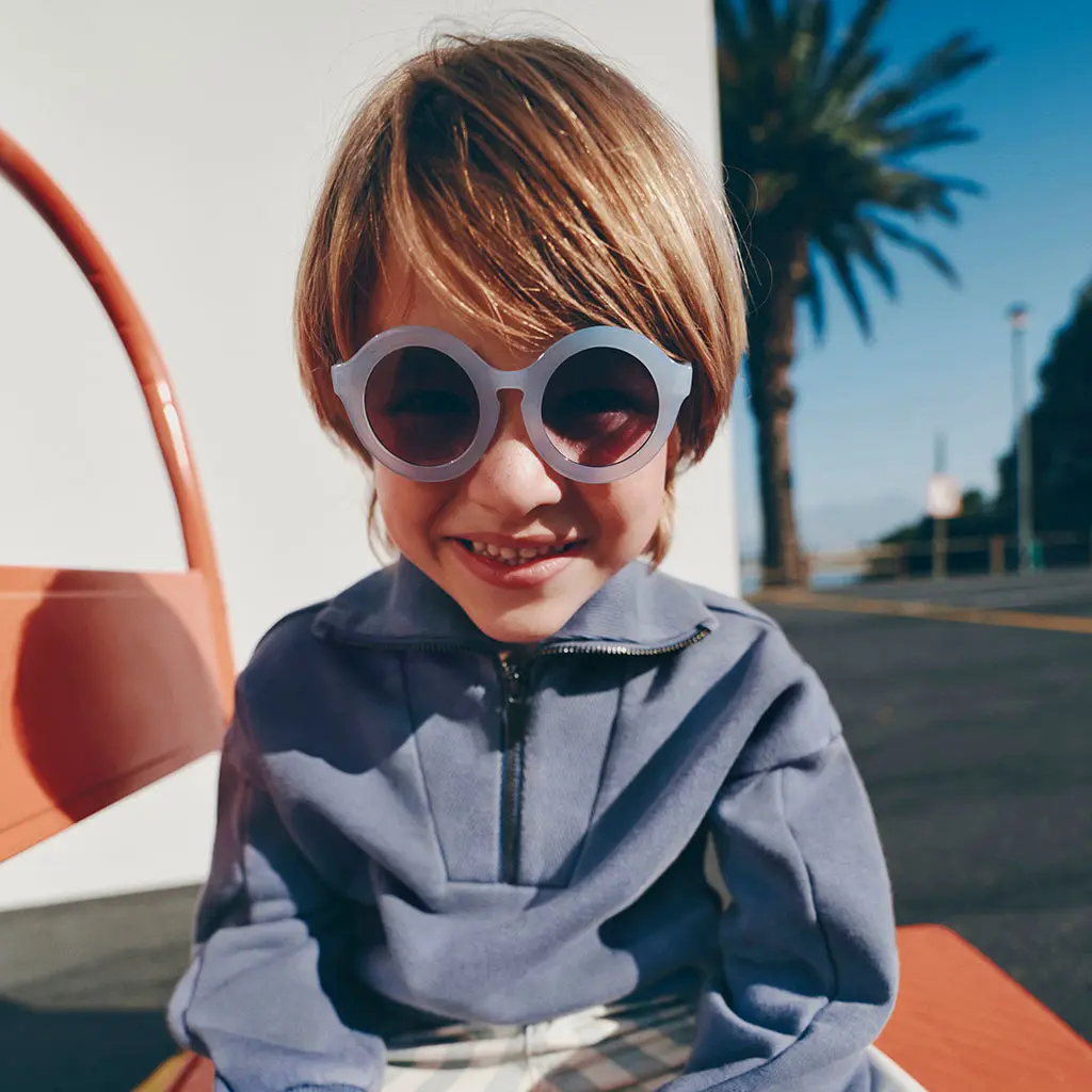 Boy wearing blue sunglasses with a blue sweatshirt and striped shorts
