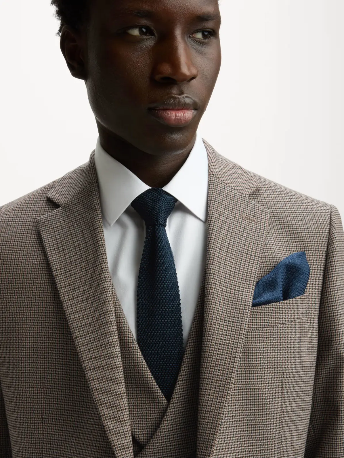 Man wearing checked brown blazer over matching waistcoat, white shirt and a navy tie with blue pocket square