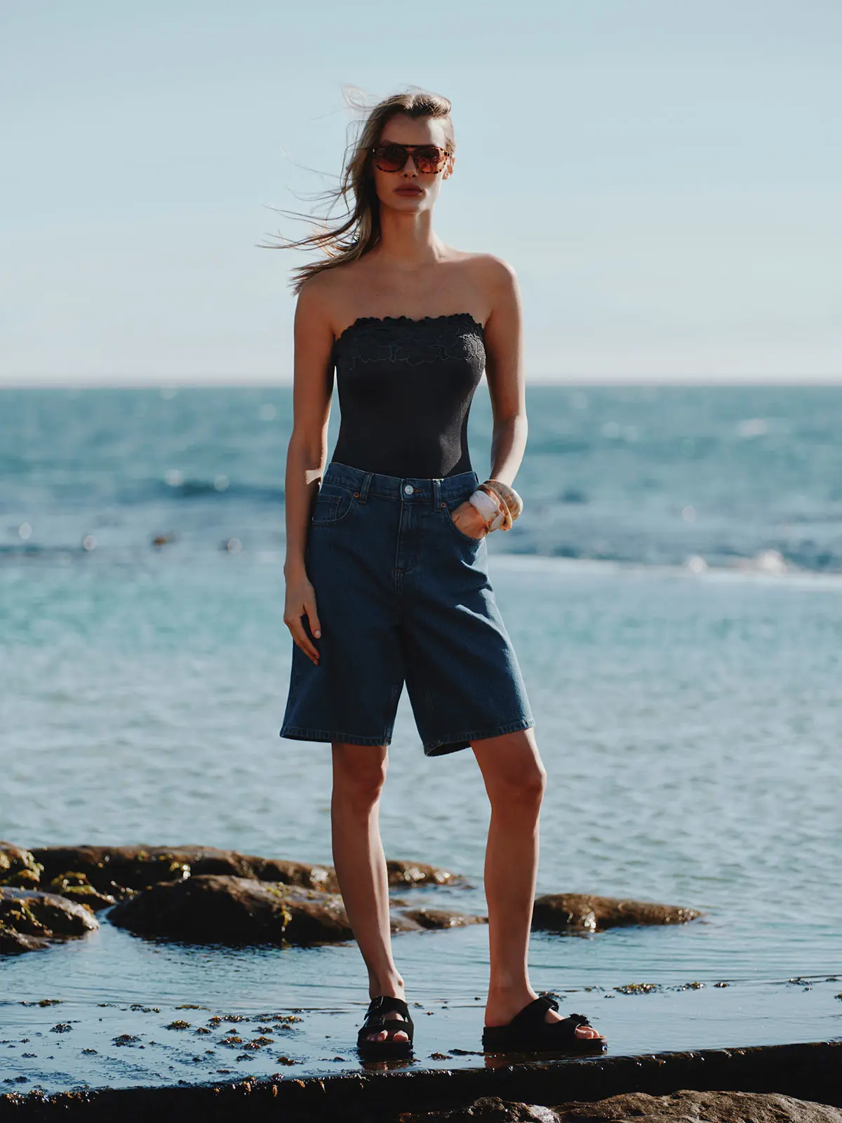 Woman wearing black top with blue denim shorts and sandals 