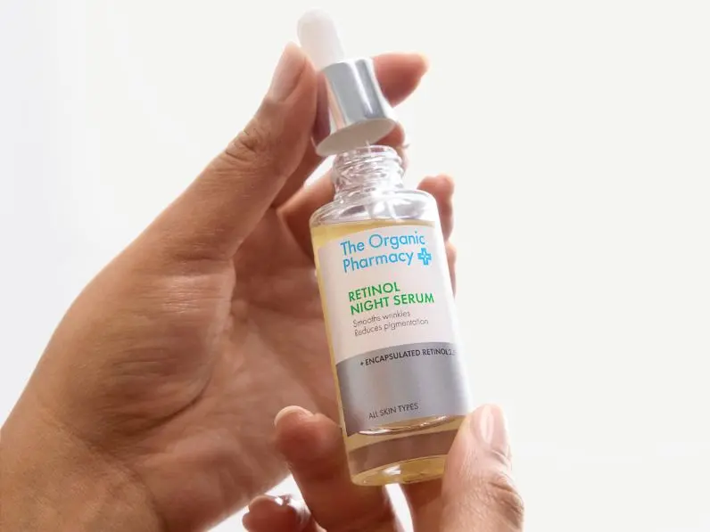 A close up of a bottle of retinol serum with a person's hands holding it