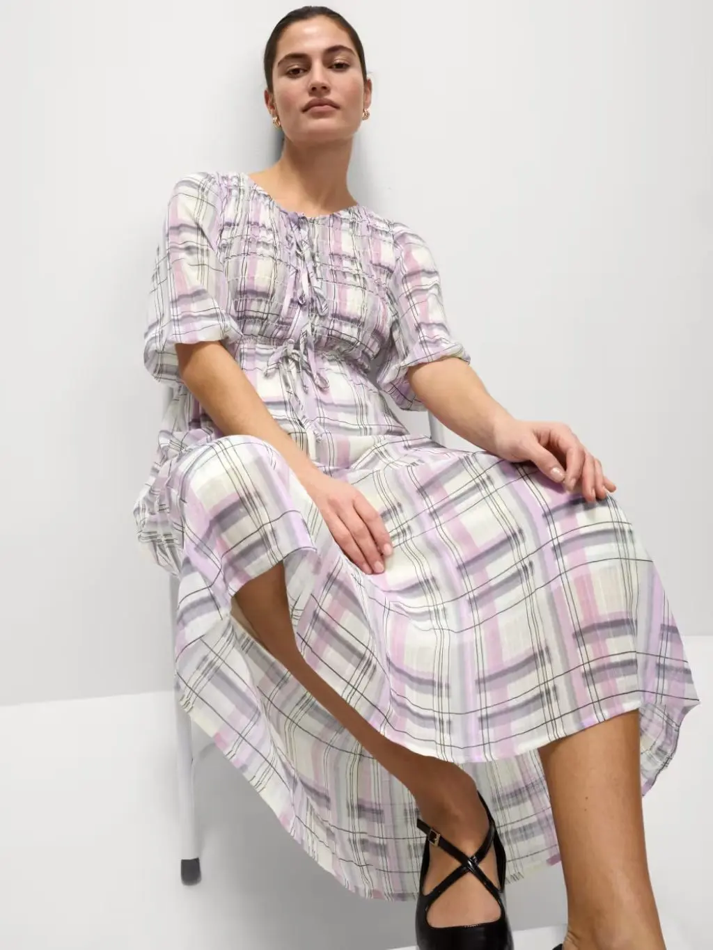 A woman sat on a chair wears a lilac check dress