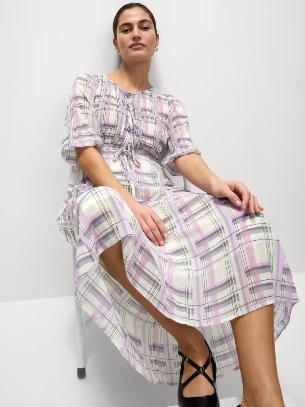 A woman sat on a chair wears a lilac check dress