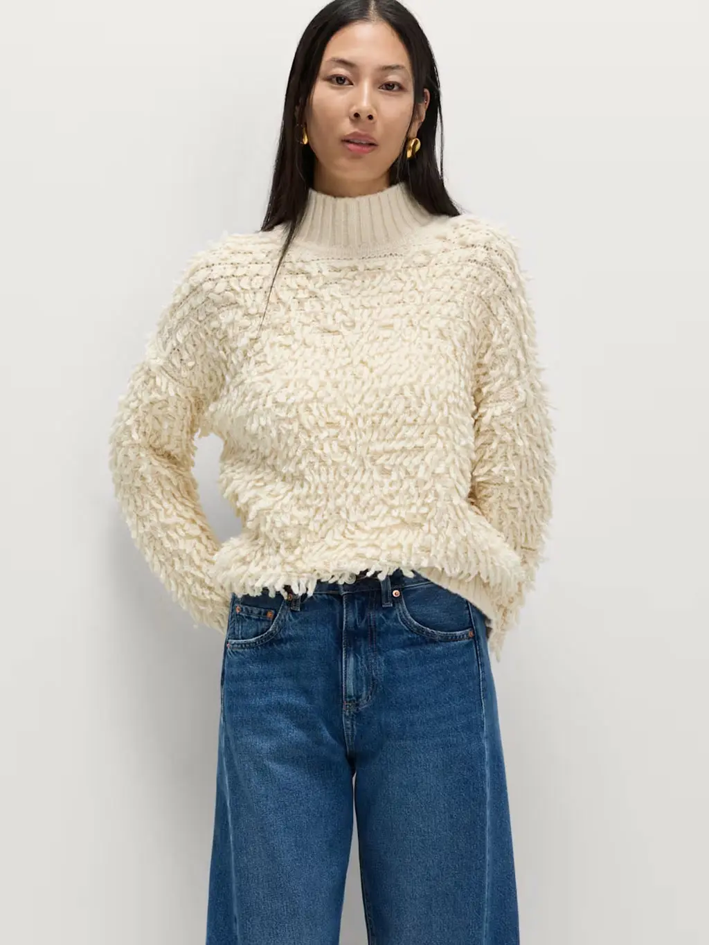 Woman wearing a cream bobble jumper with blue wide-leg jeans and gold earrings