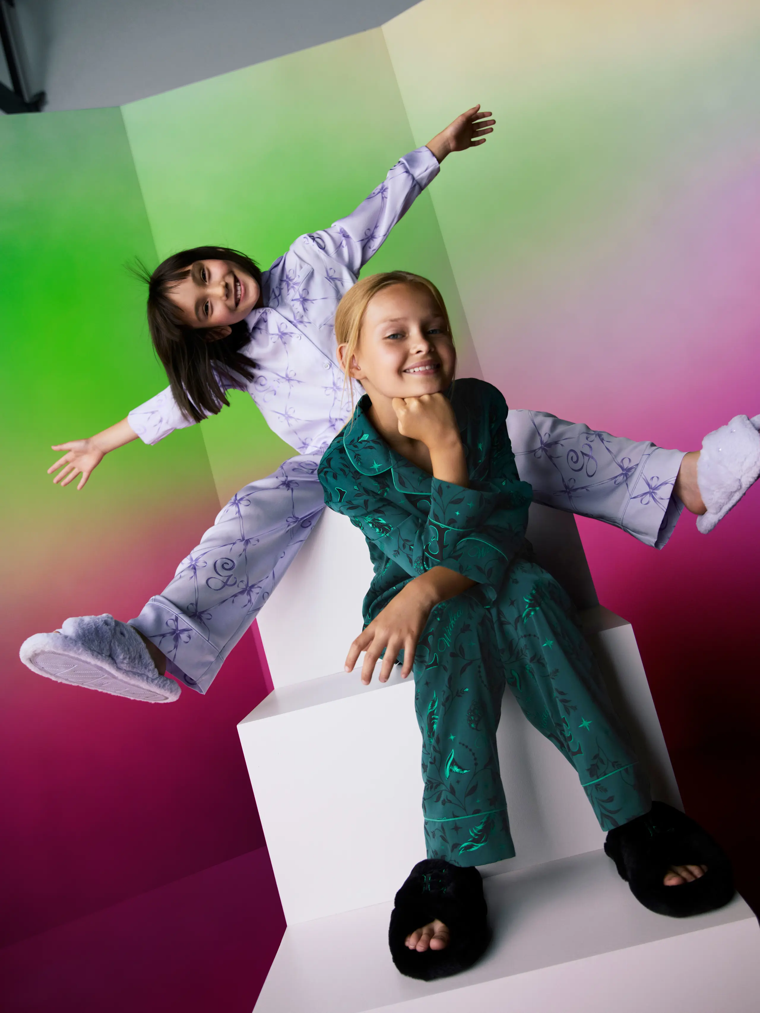 Image of two girls in Wicked themed pyjamas in lilac and emerald green