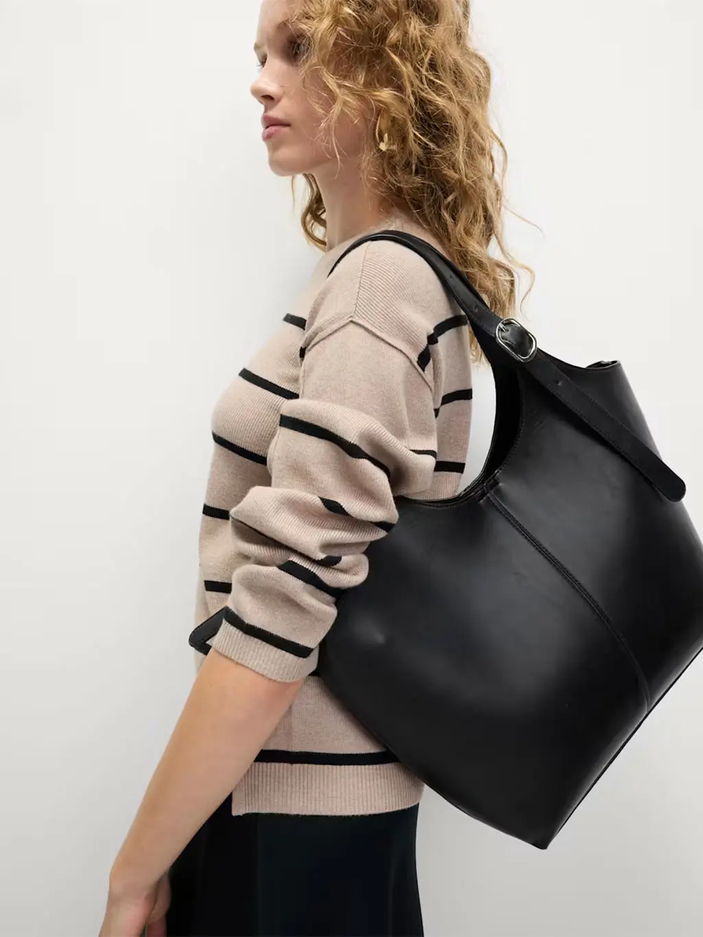 Woman wearing a striped jumper, black trousers and black leather tote bag.