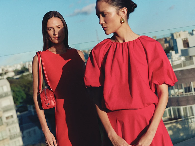 Two women wearing red dresses on a rooftop