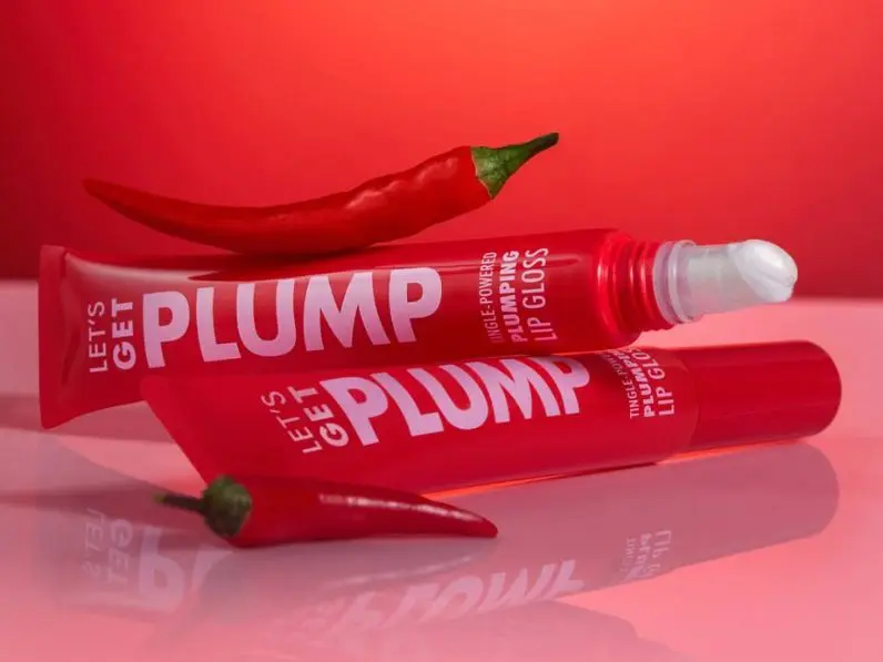 Two tubes of Let's Get Plump lip gloss, shot on a red background with two chilli peppers 