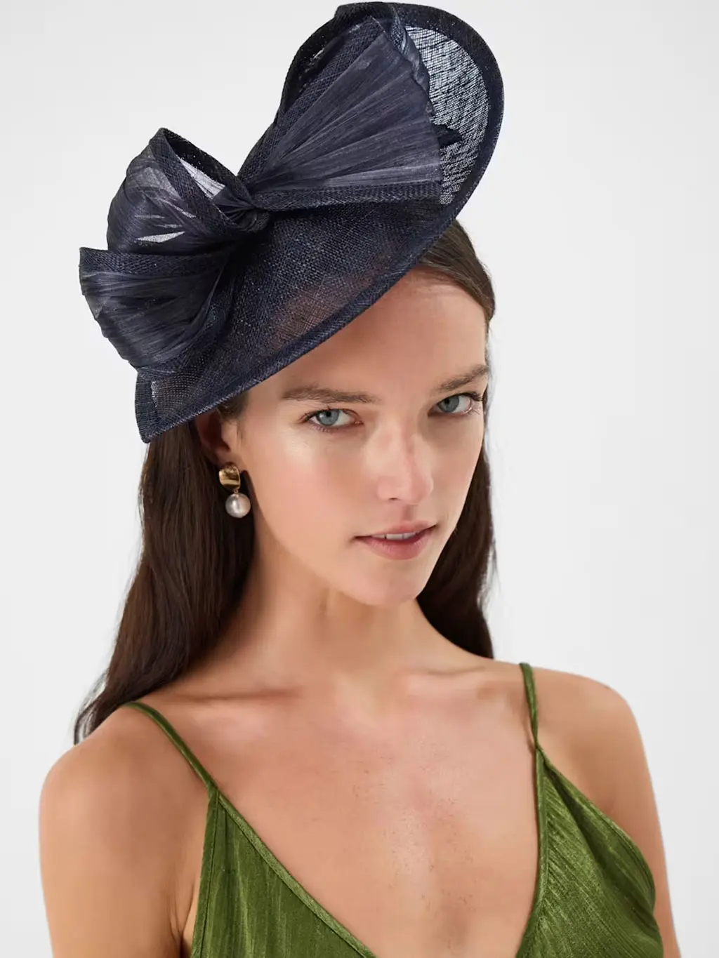 Woman wearing a green dress with a navy fascinator and drop pearl earrings