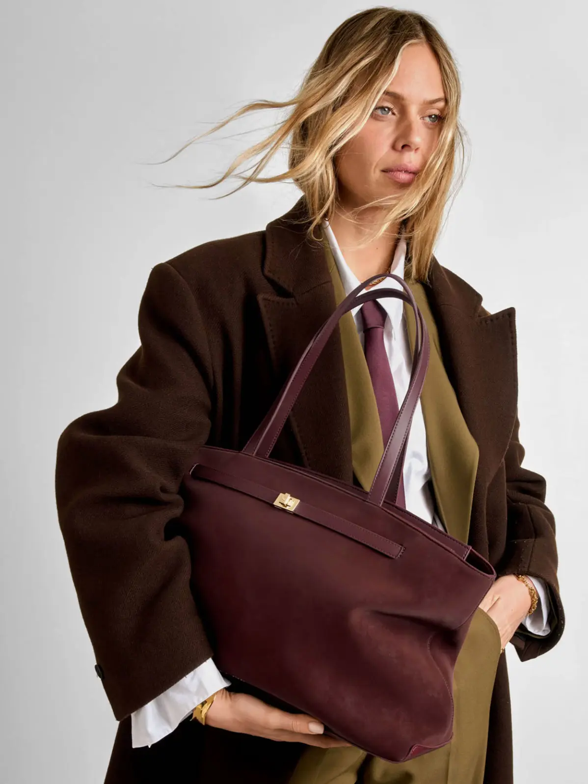 Woman wearing workwear in earthy tones, holding a suede cherry-coloured tote bag 