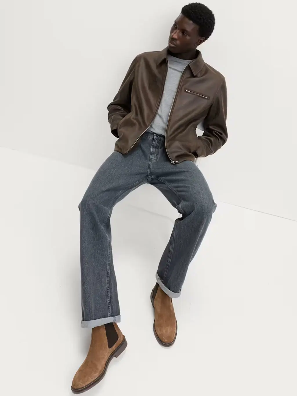 Man wearing a grey T-shirt with grey jeans, brown leather jacket and Chelsea boots