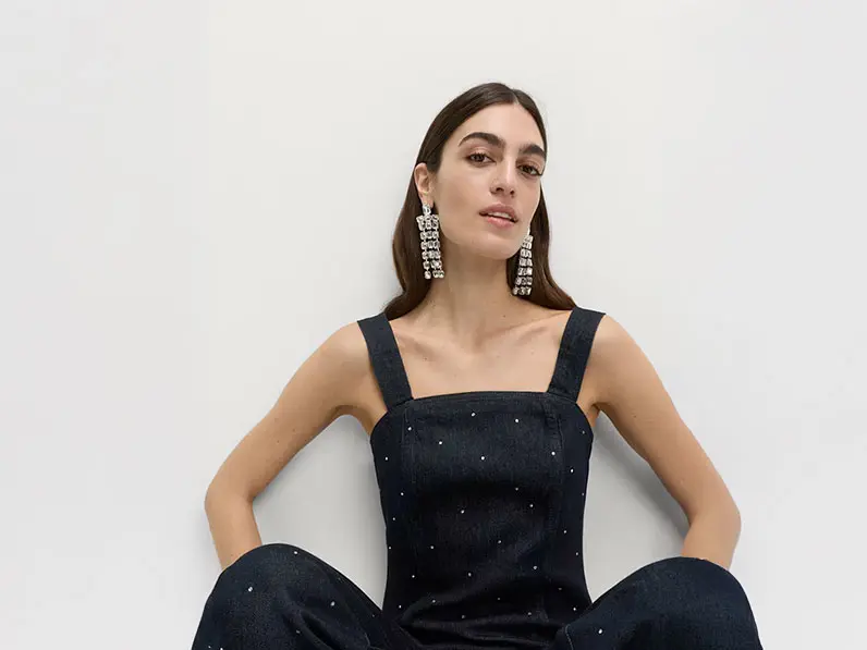 Woman wearing a studded denim top and jeans with crystal drop earrings