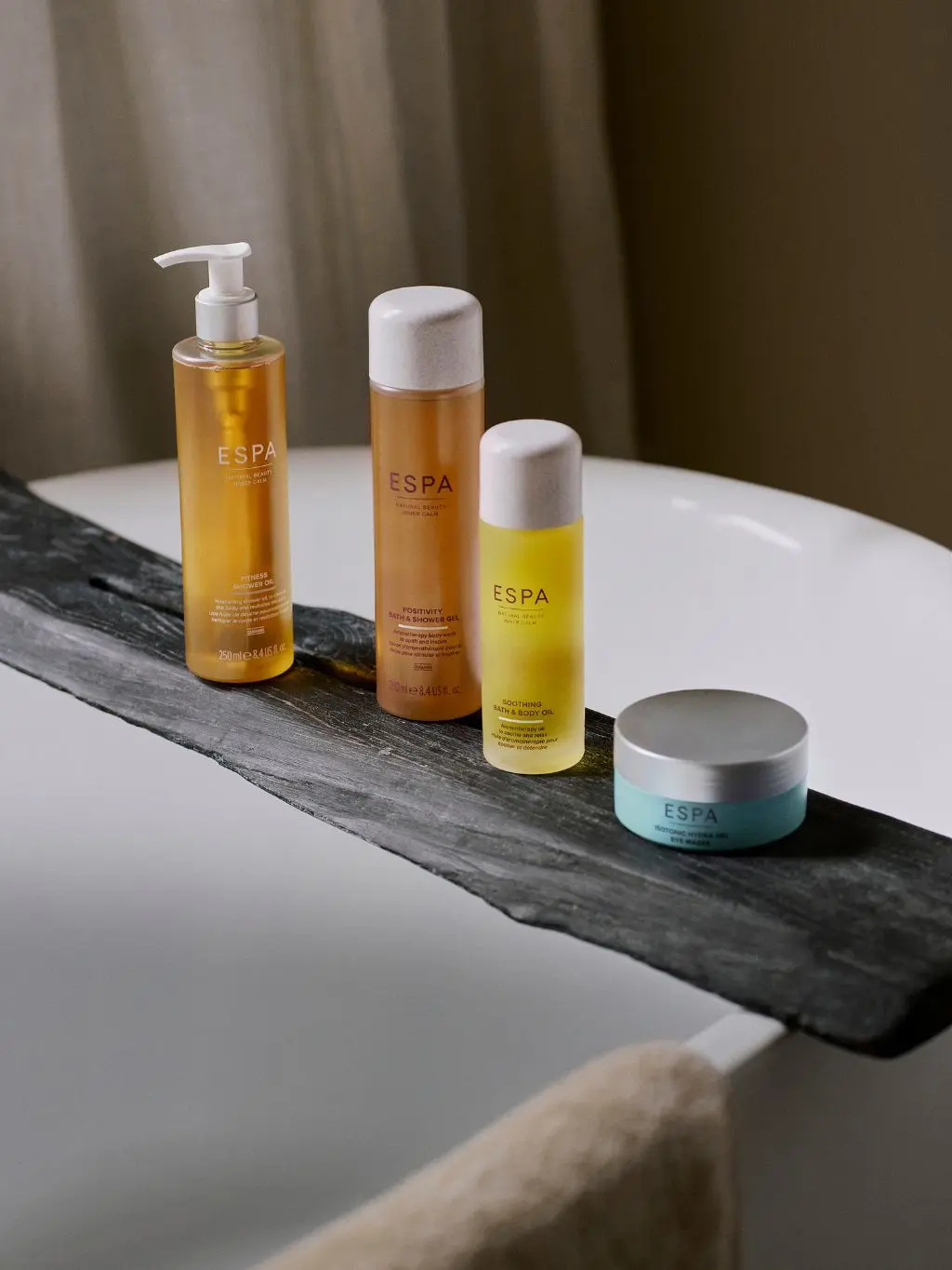An array of ESPA beauty products sit on a grey slate over a roll top bath