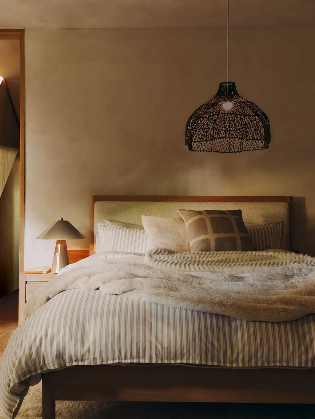 Neutral bedroom with green and white striped bedding and cosy faux fur throw.