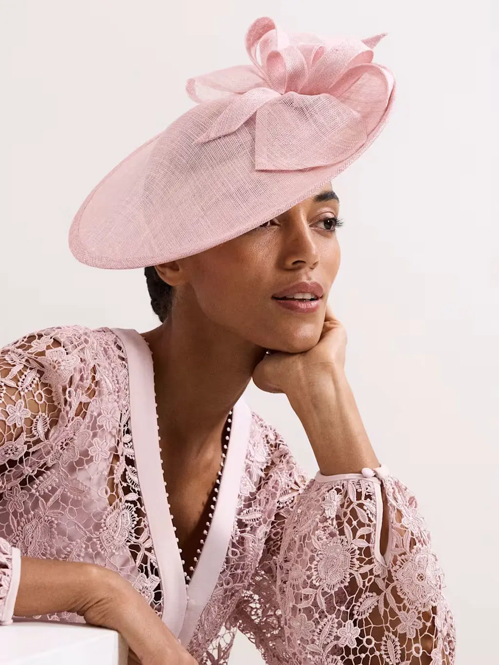 Woman wearing a pink fascinator with a coordinating lace dress