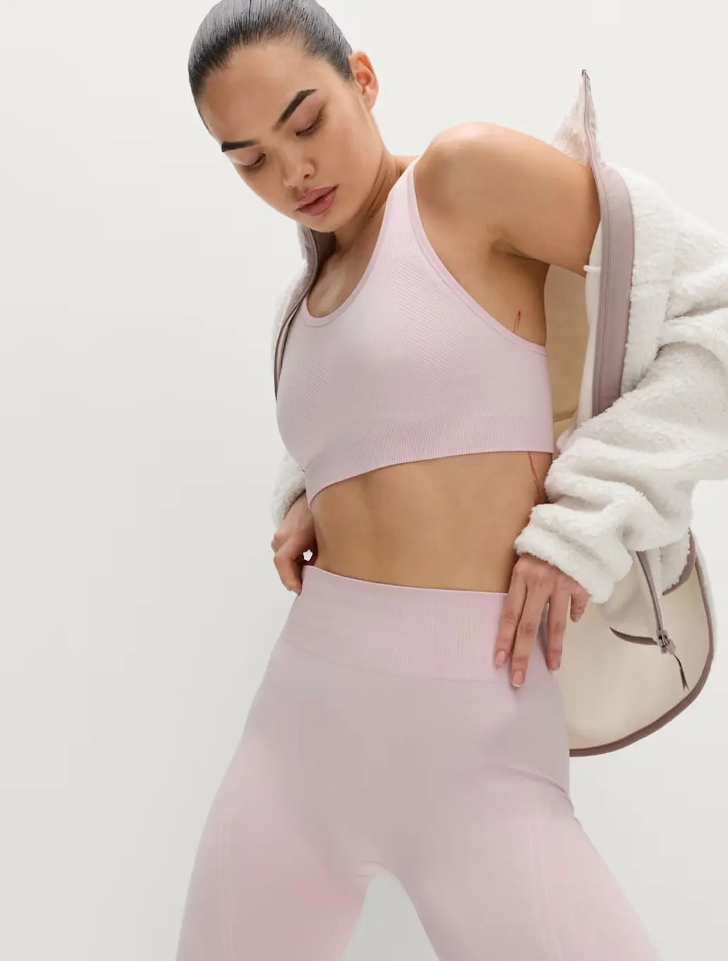 Woman wearing a pink seamless sports bra with matching leggings and a fleece jacket