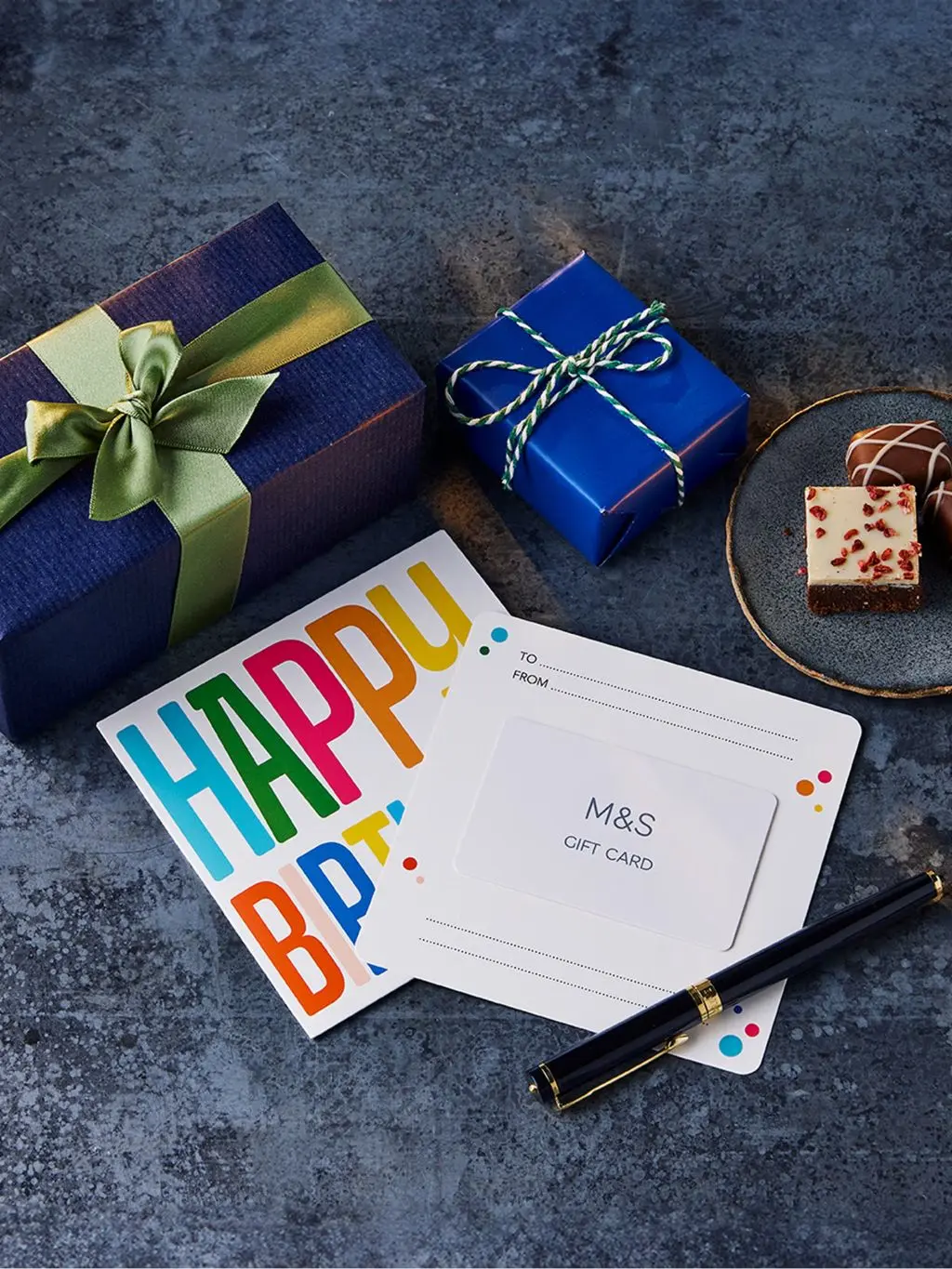 A shot showing an M&S birthday gift card, alongside a wrapped gift and a slice of cake