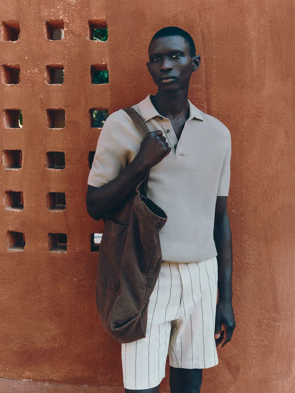 Man wearing light polo, linen shorts, and brown tote bag