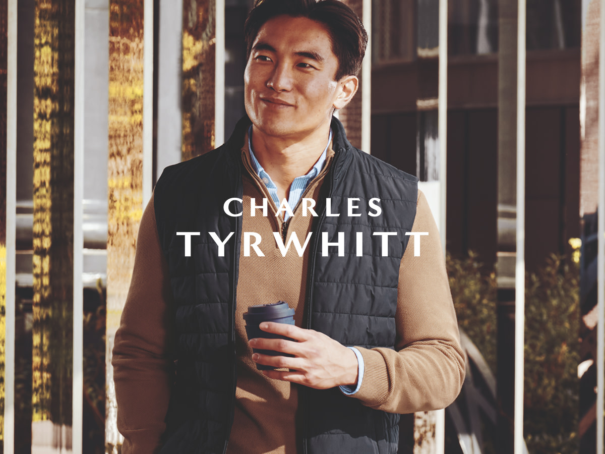 Man wearing black Charles Tyrwhitt gilet and camel zip-neck jumper, holding a coffee cup