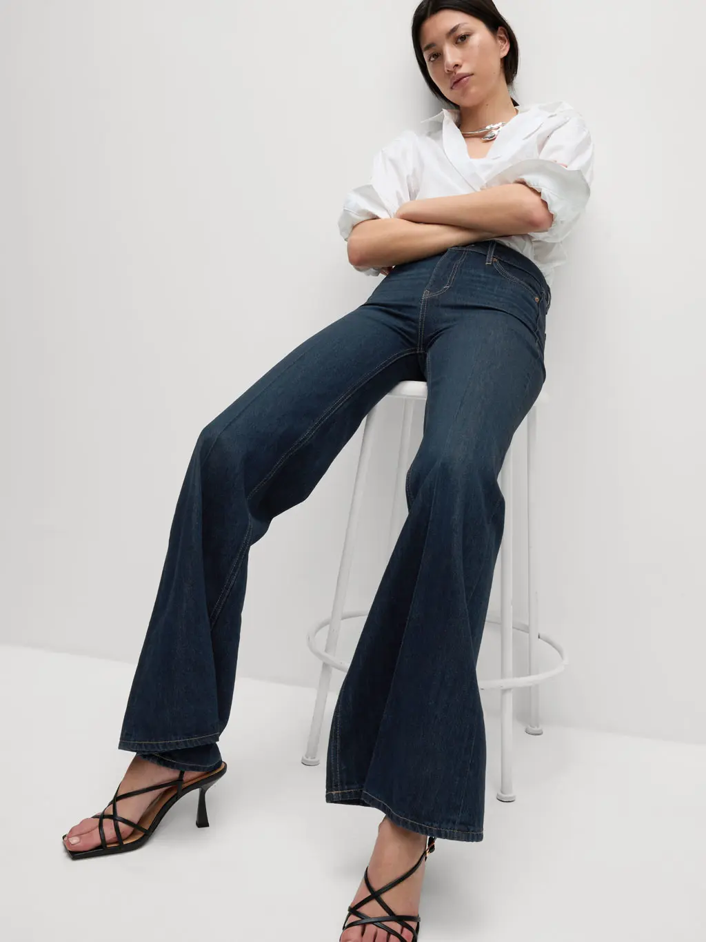 Woman wearing flared dark wash jeans, a white shirt and heels