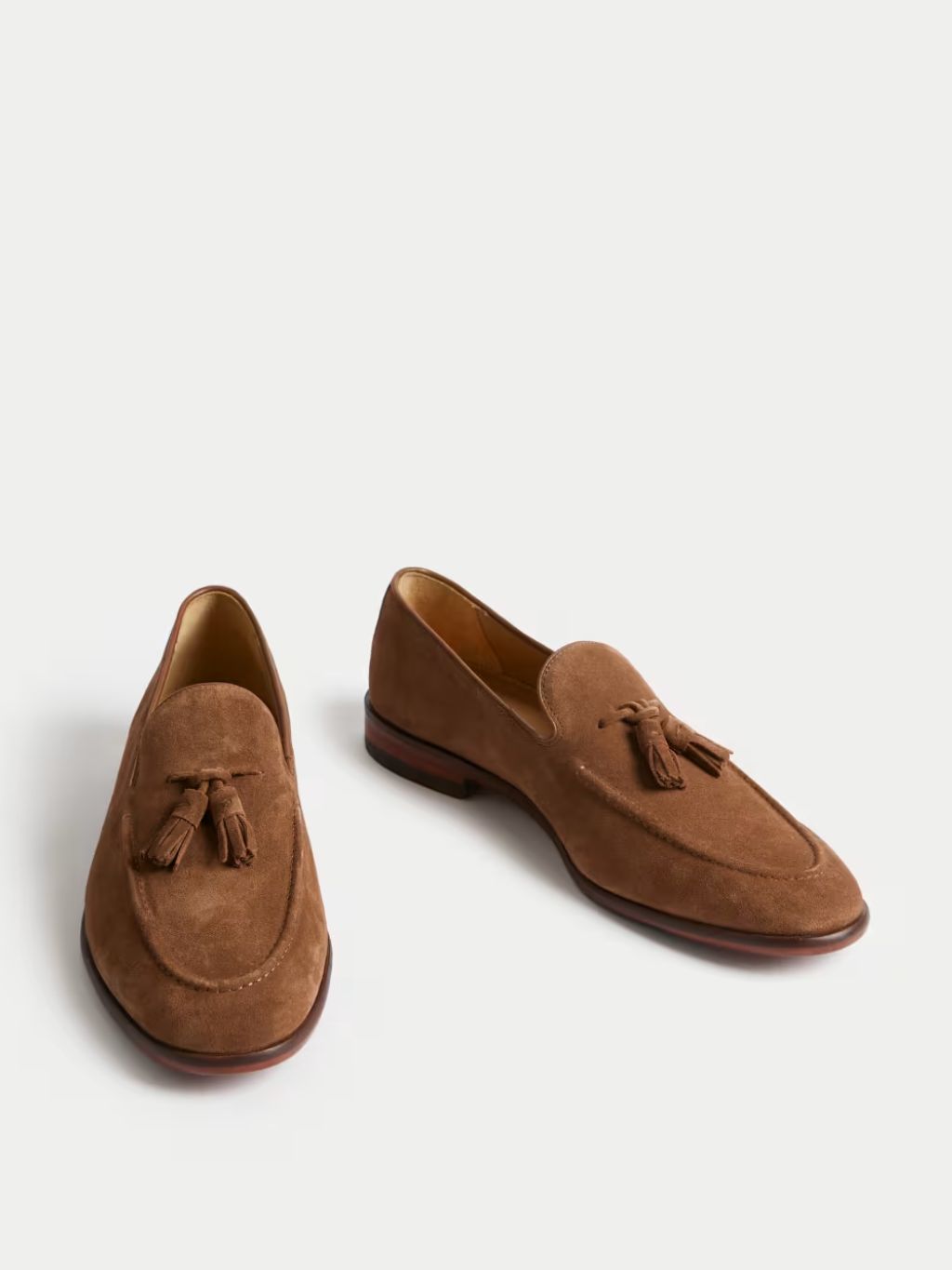 A still life of brown tasselled suede loafers on a light background