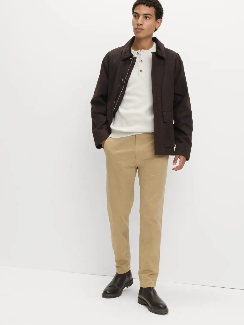 A man wears beige chinos, a brown jacket and Chelsea boots