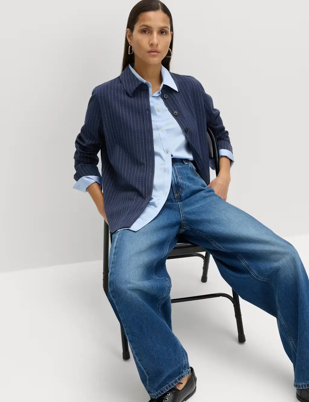 Woman wearing navy pinstripe shirt, light blue shirt and deep blue jeans