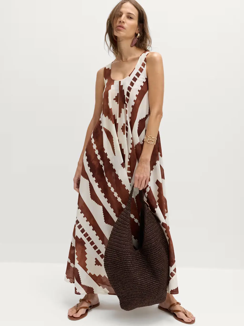 Woman wearing a brown and white geometric-print dress with brown sandals and a woven bag
