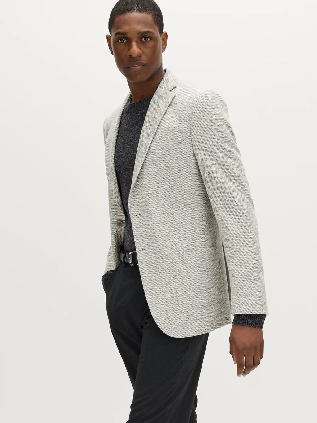 Man wearing a grey jumper and navy trousers with a light-grey blazer