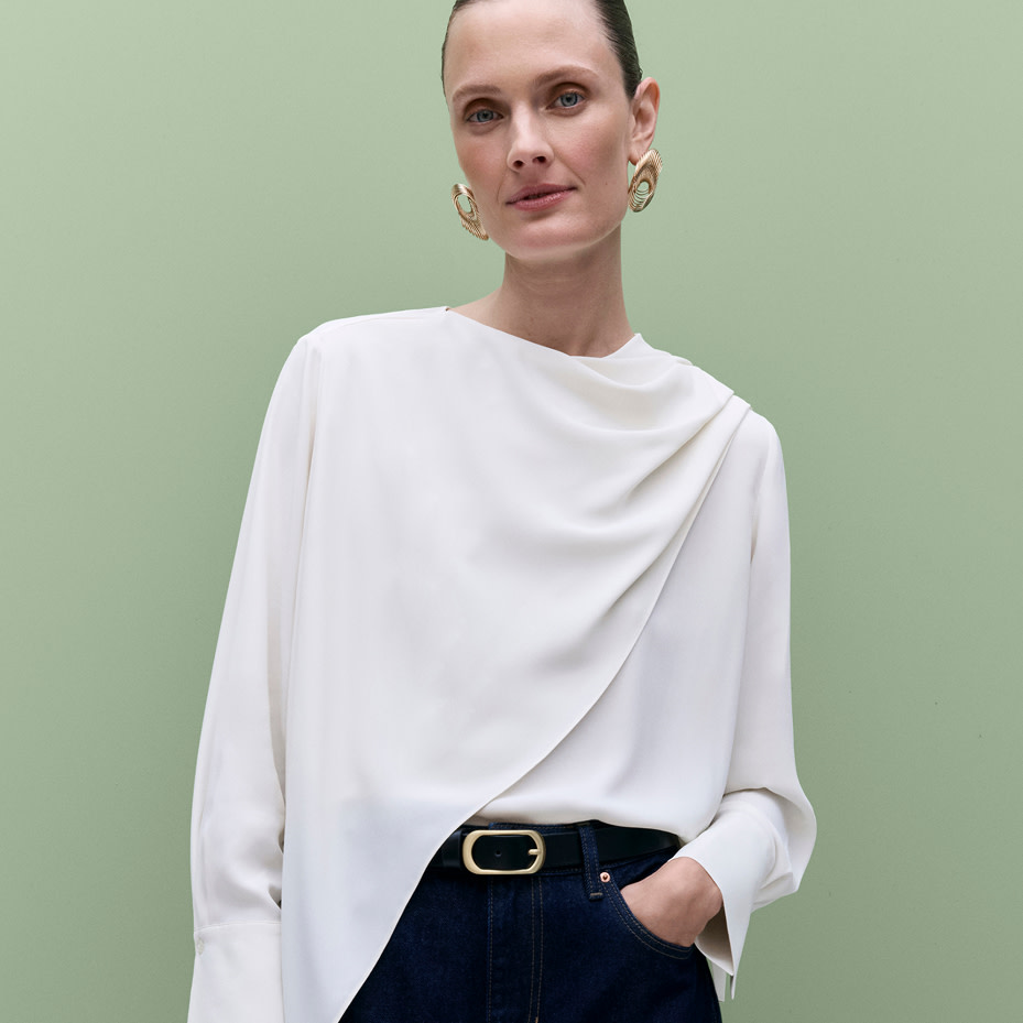 Woman wearing white draped top, black belt with gold buckle detail and black jeans 