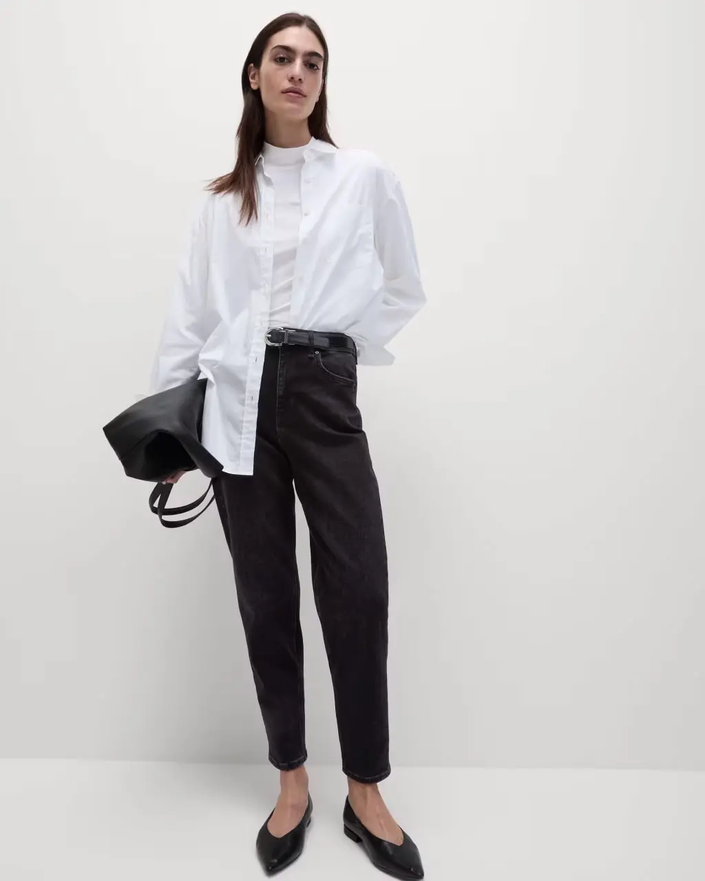 Woman wearing black mom jeans with a white T-shirt, white shirt, black ballet pumps and a black bag.