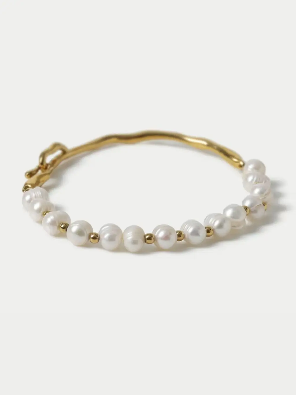 A cutout of a gold and pearl bracelet shot against a light cream background