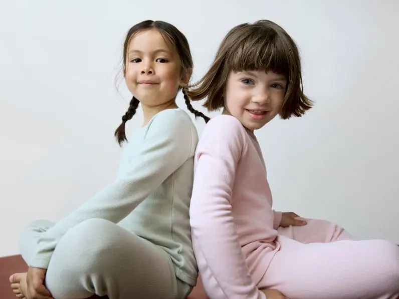 Two girls sit back to back wearing mint green and pastel thermals