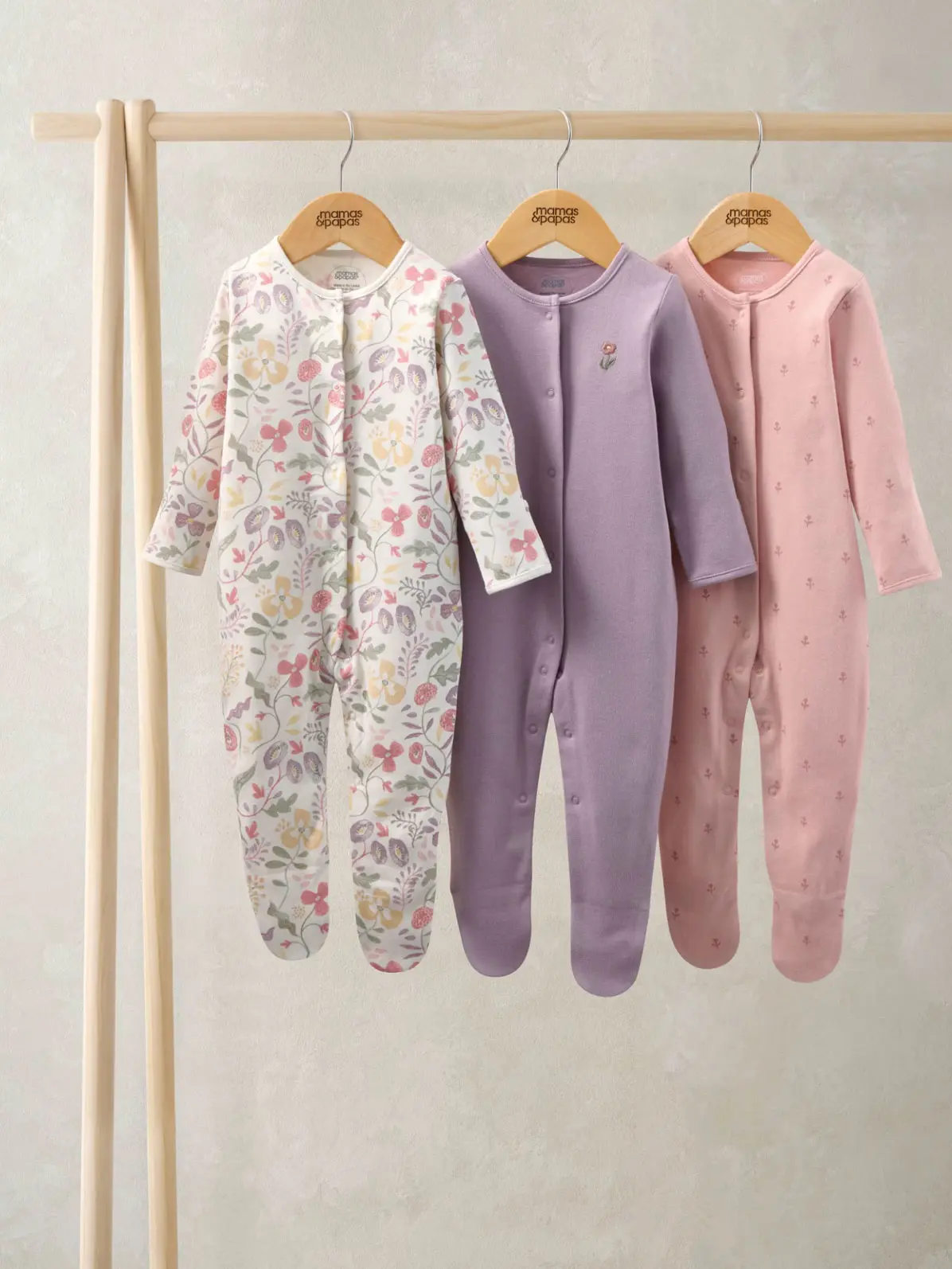 Three floral sleepsuits hung up on a rail 