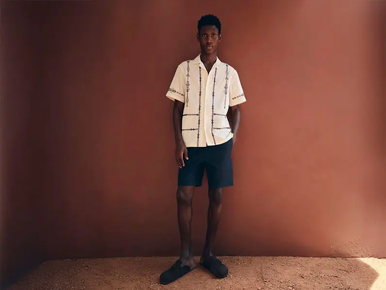 Man wearing an embroidered linen shirt with navy shorts and clogs