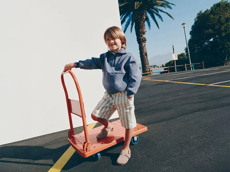 Boy wearing blue sweatshirt with striped shorts and sandals