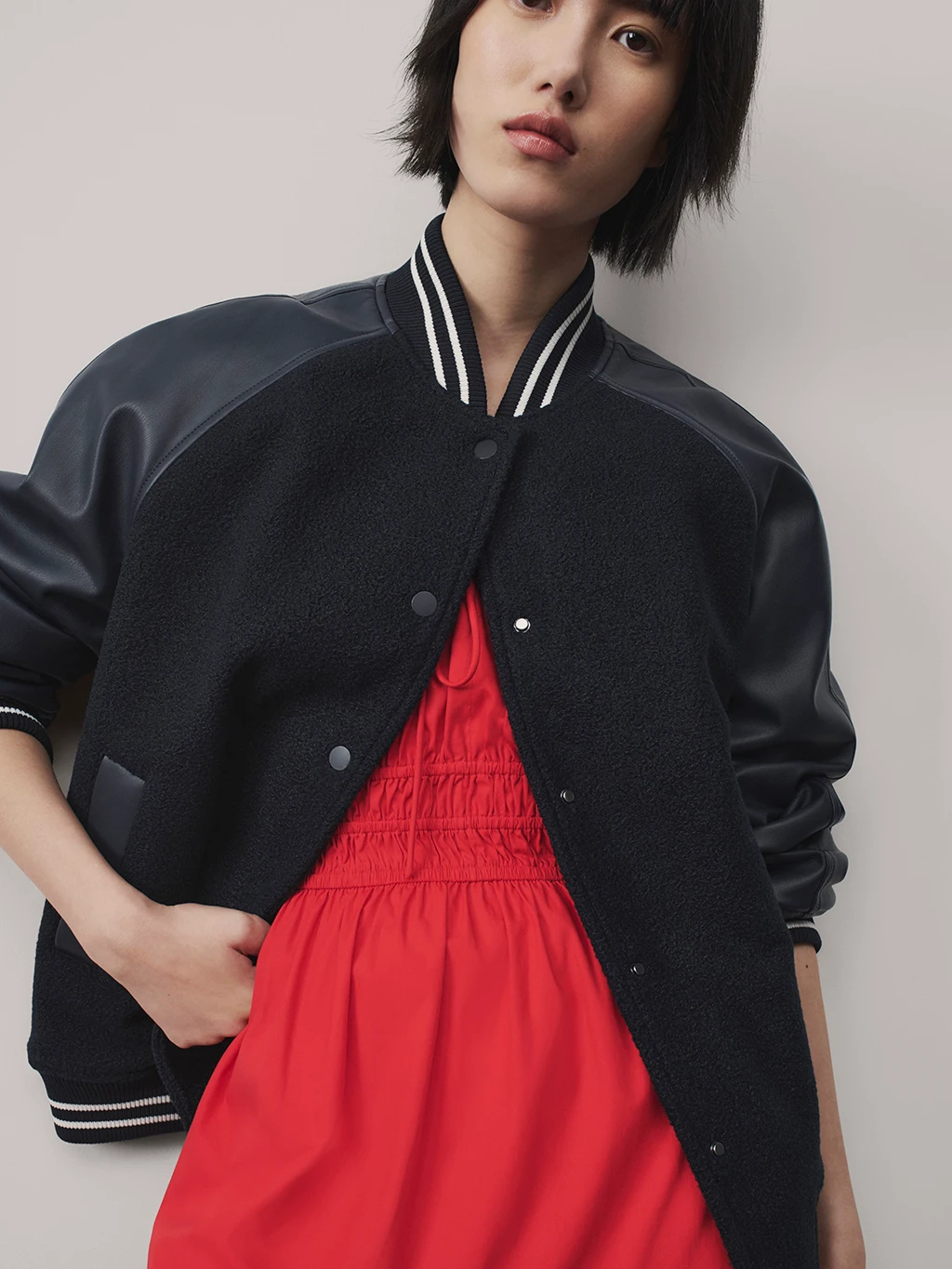 Woman wearing black varsity jacket and a red smocked dress