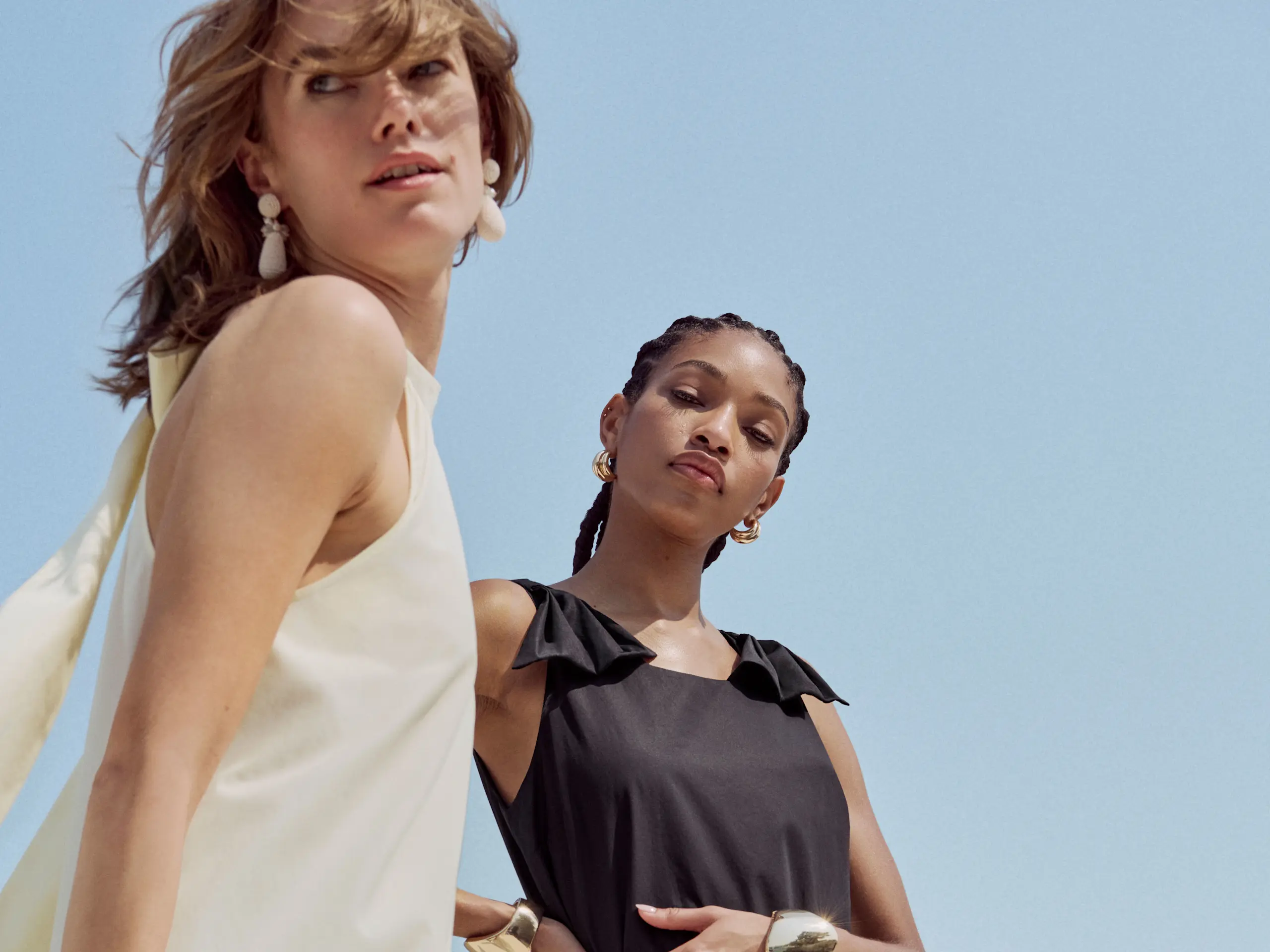 One woman wearing a cream dress, second woman wearing a  black dress. 
