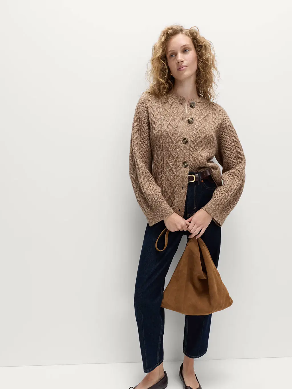 Woman wearing a cable-knit cardigan with blue jeans and ballet pumps