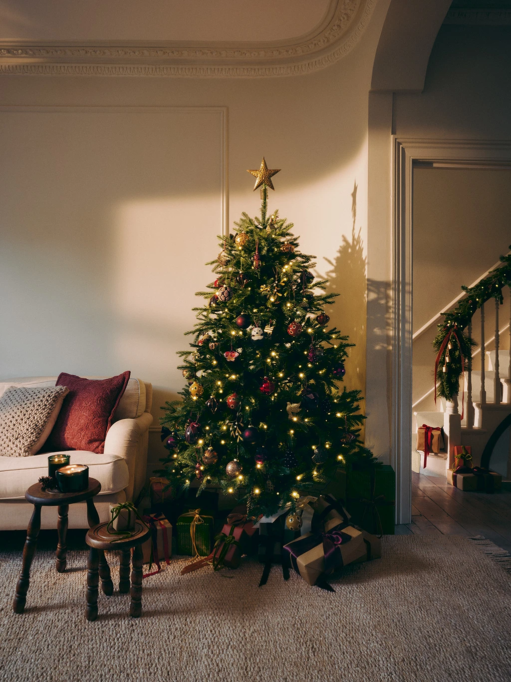 Christmas tree decorated with red and gold baubles surrounded by presents and two small stools.