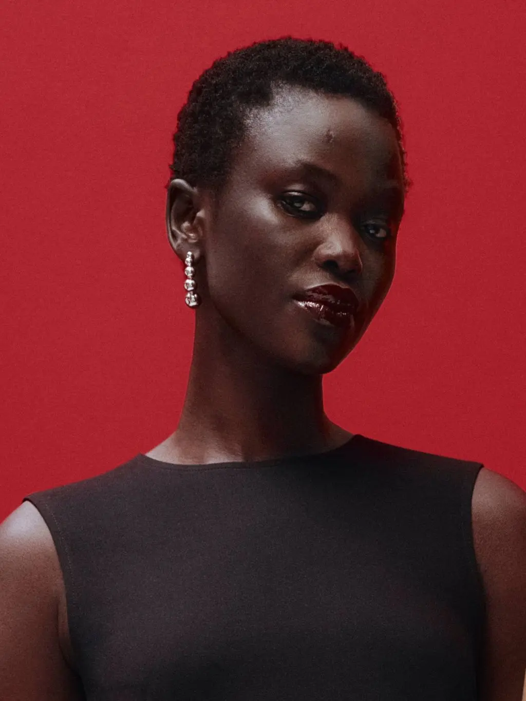 A woman wears dark burgundy lipstick, a black top and dangly earrings