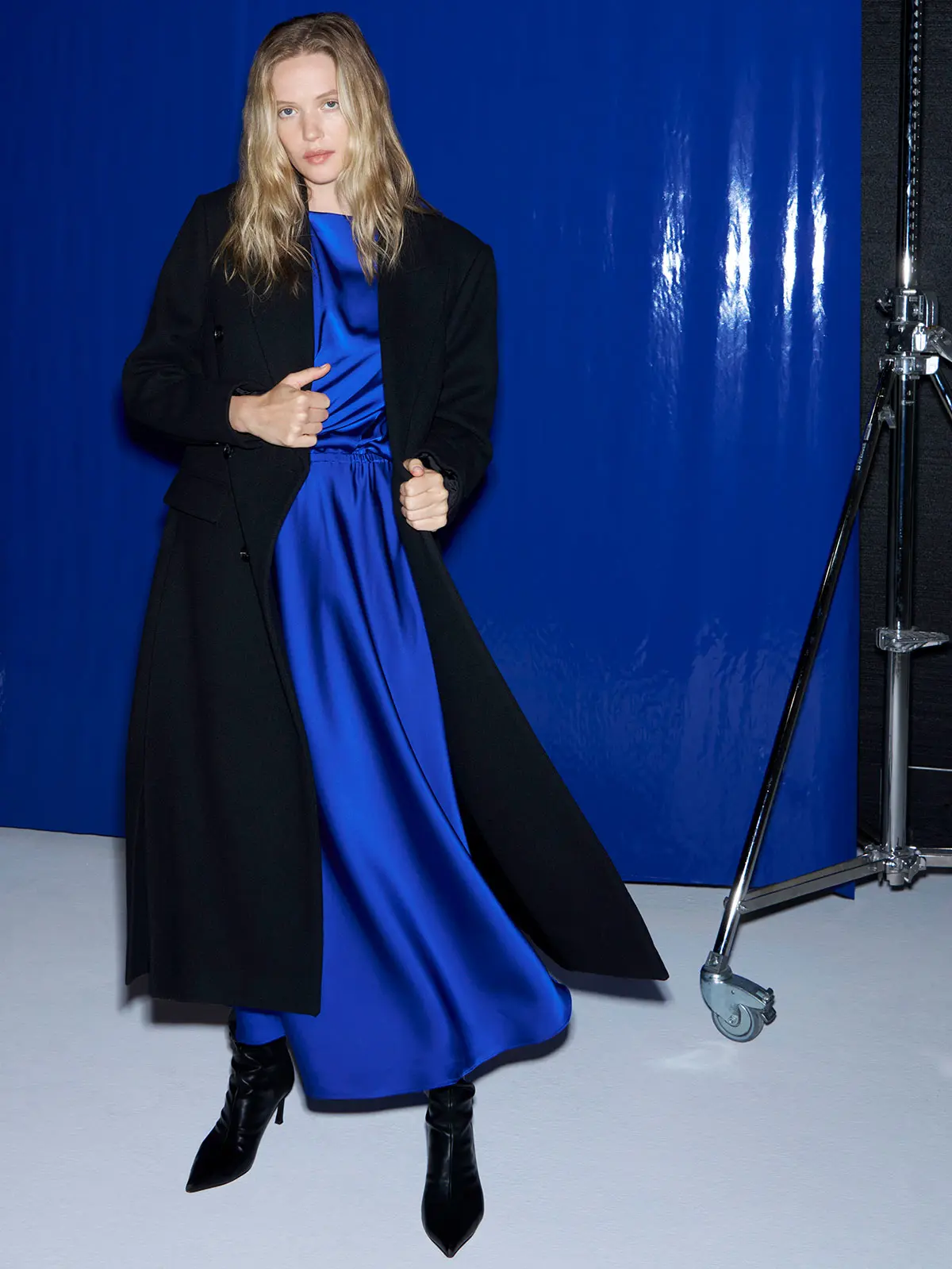 Woman wearing black coat over blue satin dress, paired with heeled boots