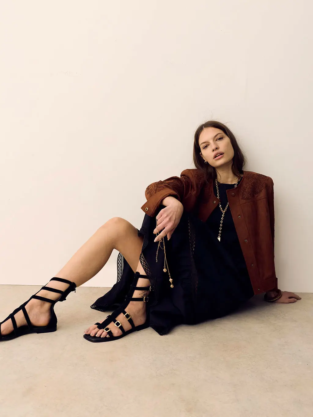 Woman wearing a black maxi dress with an embroidered suede jacket, black sandals and layered jewellery