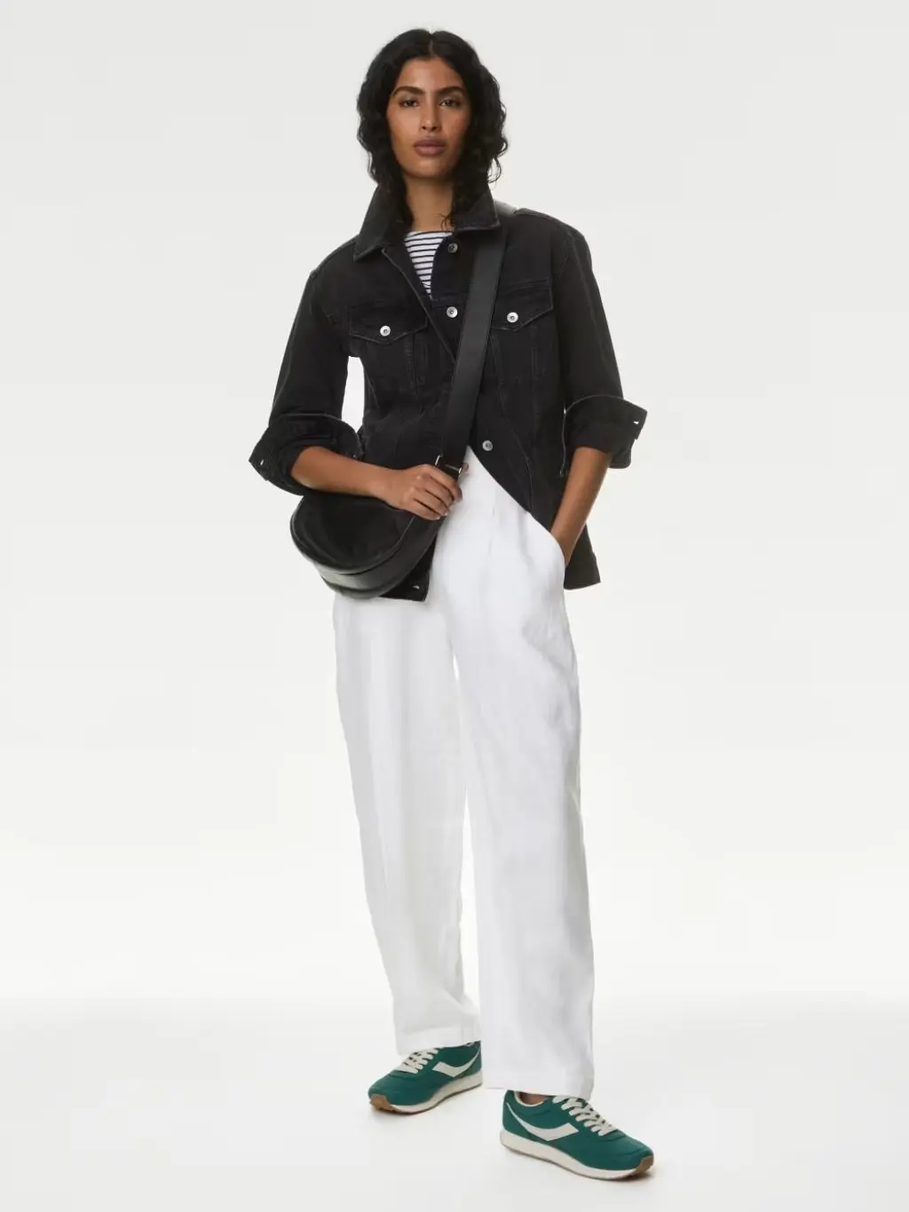 A woman wears a denim jacket and white linen trousers with trainers