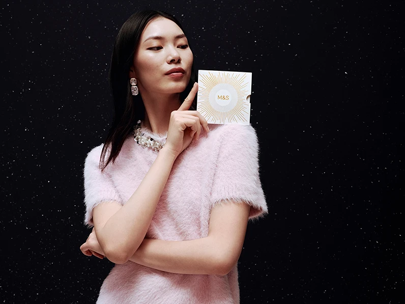 Woman wearing a pink jumper holding an M&S gift card