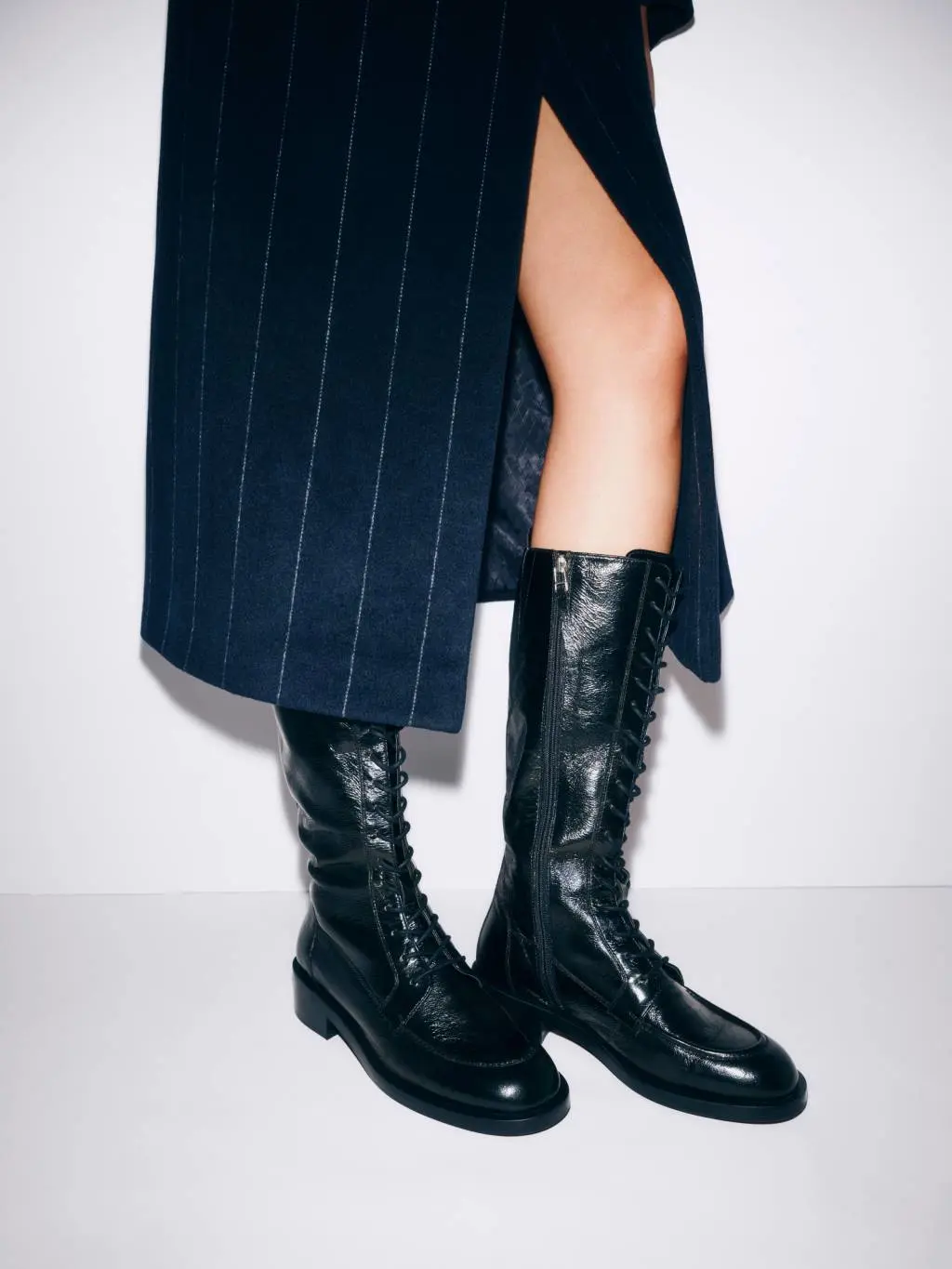 A woman's legs wearing knee high lace up boots and a long midi skirt with a split in it