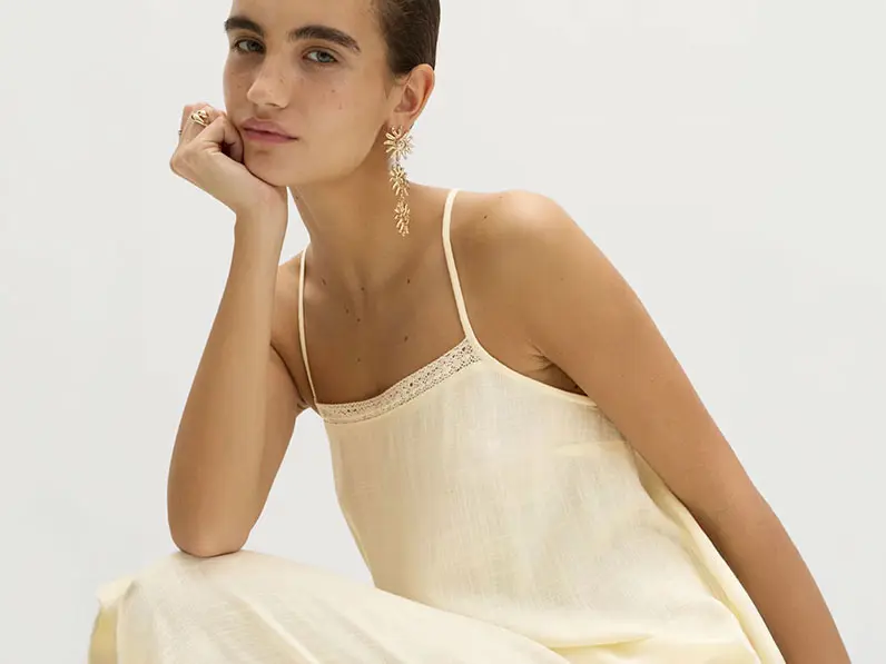 Woman wearing a cream linen maxi dress with gold drop earrings and stacked rings