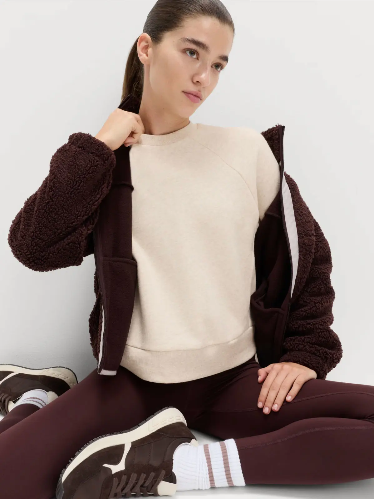 Woman wearing brown leggings, cream sweatshirt, brown jacket and brown trainers 