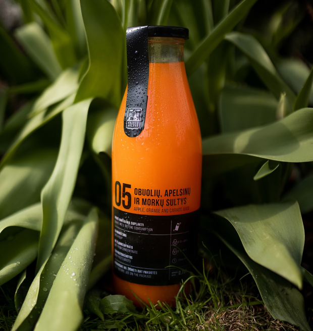 Apple, orange and carrot juice bottle placed on grass in front of foliage