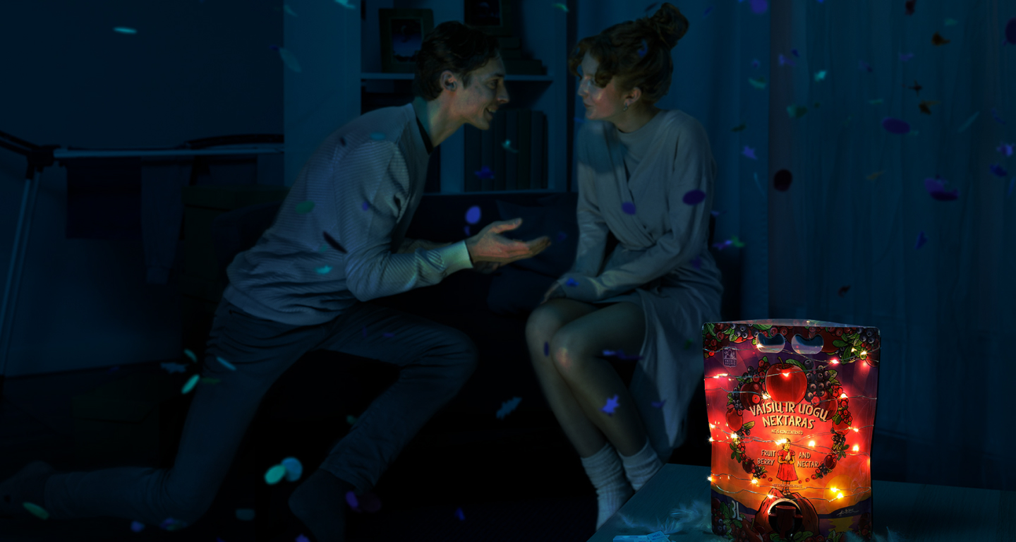 Image of a couple sitting and smiling together in a dimly lit apartment and a fairy tale pouch lit by small lights in the front of them.