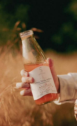 An image of a glass bottle of Sequoia tea drink held by hand in front of the background of grain field